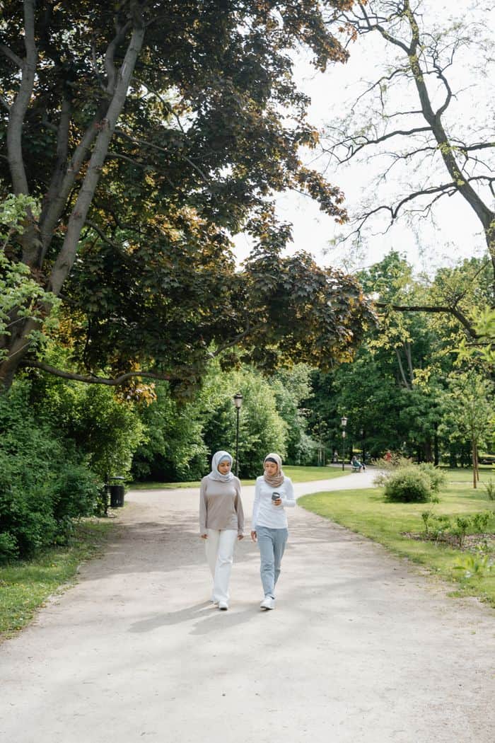 services-03 Two Muslim women in hijabs walking together in a scenic park, showcasing friendship and nature.